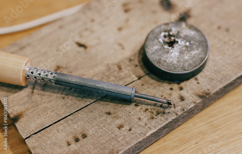 Close-up of a soldering iron and metal piece on a wooden surface in a workshop. Hobby