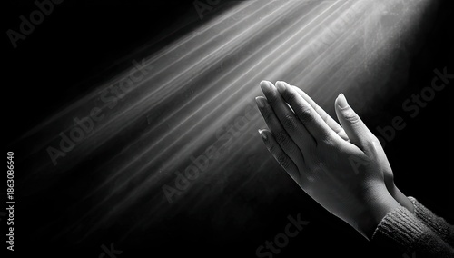 A grayscale shot of hands clasped in prayer, illuminated by heavenly light