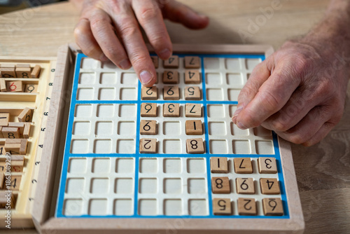 Fotografia closeup hands carefully placing number into Sudoku puzzle, senior man focused on