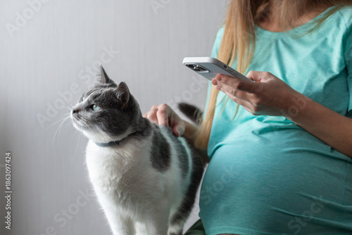 Foto Pregnant woman messaging on a telephone and petting a cat.