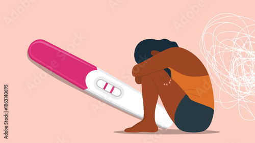 A disheartened woman sits alone on the floor next to a negative pregnancy test result