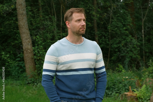 Handsome young man standing outdoors. Male thinking looking around feel happy, calm and serious. Green park background. Guy business employer, businessman manager inspired in nature. Diversity People