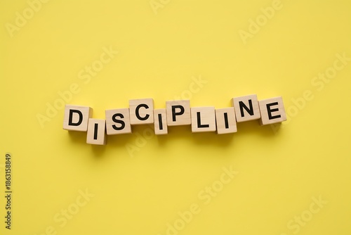 Wooden blocks spelling DISCIPLINE, loosely arranged on  bright yellow background, minimal leadership concept photography.