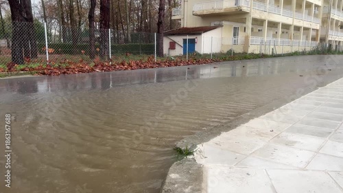 Rainwater flowing on urban street with rippling puddle near buildings