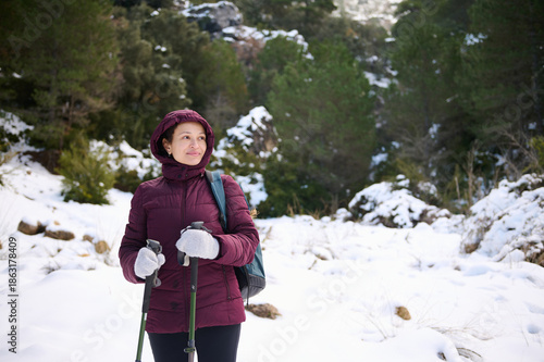 Woman Hiking In Snowy Forest With Walking Poles On Winter Trail