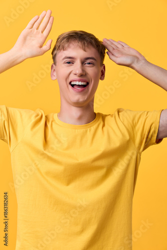 Obraz na płótnie Joyful, cheerful man in a yellow shirt raises hands in a bright studio, exuding