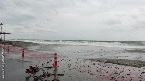 Stormy beachside waves crashing against red pavement amid overcast skies