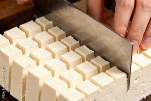 Knife creating a waffle-cut pattern on a block of  tofu, close-up.