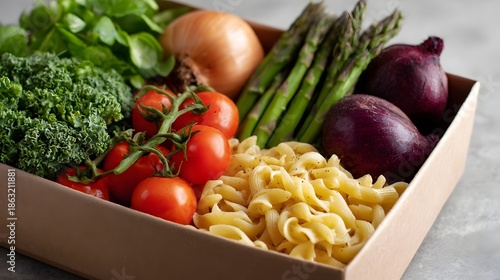 Fresh ingredients for a healthy meal kit including pasta tomatoes kale asparagus and onions in a cardboard box