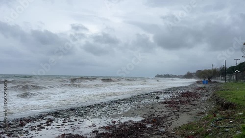 Stormy coastal waves crash on rockstrewn shoreline under overcast sky