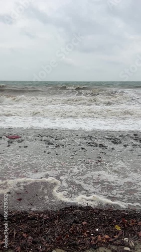 Stormy coastal waves crashing on pebble shoreline under overcast skies