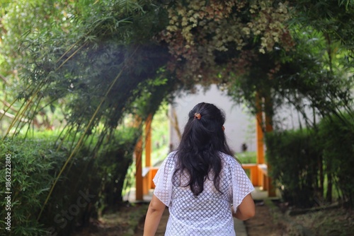 Woman walking through a green garden walkway in Kuala Lumpur, Malaysia, framed by plants and arches, expressing calm travel exploration.