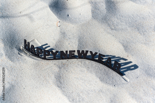 A black and white sign on a sandy beach that says Happy New Year
