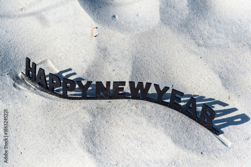 A black and white sign on a sandy beach that says Happy New Year