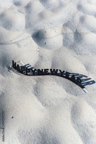 A black and white sign on a sandy beach that says Happy New Year