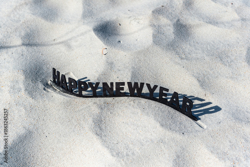 A black and white sign on a sandy beach that says Happy New Year