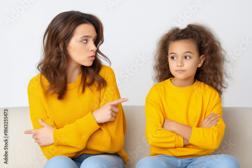Woman and girl wearing matching yellow sweaters are sitting on a couch, engaged in a serious conversation, expressing emotions and body language, showcasing a family dynamic