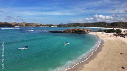 Breathtaking aerial footage flying over a pristine tropical beach, revealing stunning turquoise waters, white sandy shores, and picturesque green hills under a bright blue sky with fluffy clouds