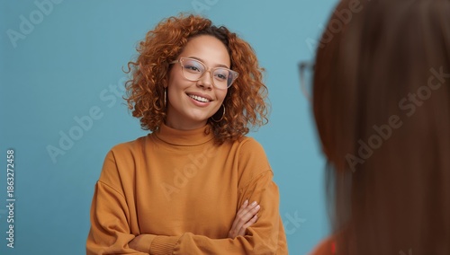 Smiling Person With Curly Orange Hair in a Blue Setting With Arms Crossed