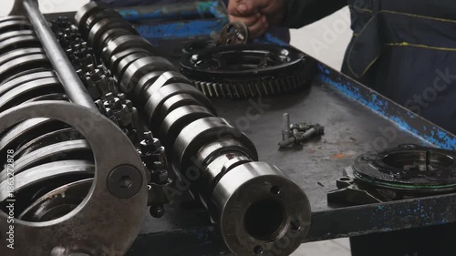 The camshaft and valve train components of a car engine. Mechanics inspect and document metal engine components. An engine mechanism on a work bench in a workshop during professional auto repair.