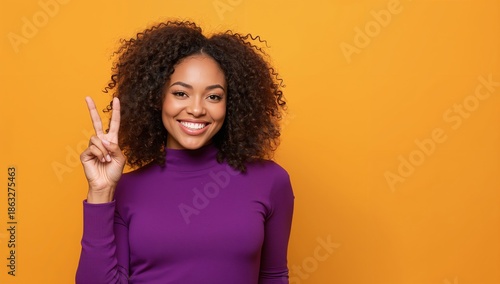 Woman With Curly Hair Makes Peace Sign in Front of Yellow Wall During Bright Day
