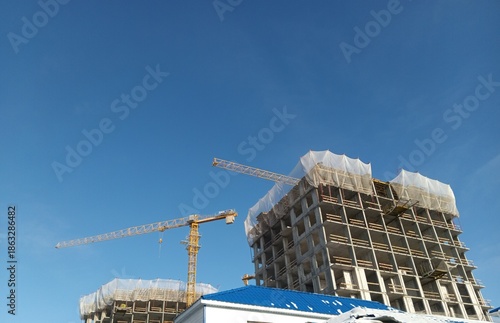 House construction site with prefabricated panels and a construction crane against a clear blue sky. Modern residential building process, industrial construction technology and urban development