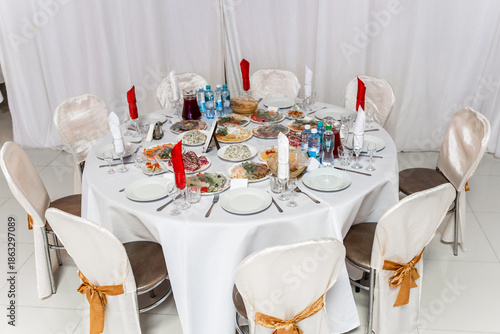 Round banquet table lavishly set for a celebration with white linen, numerous plates of cold appetizers