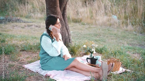 Latina woman having a picnic in the park. Using her cell phone. Country style.