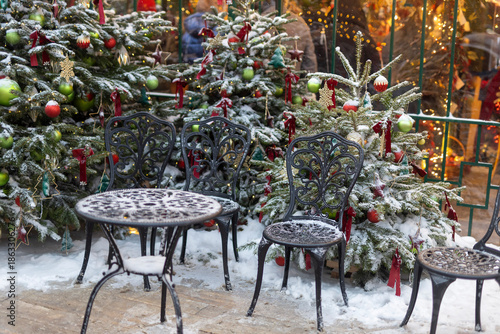 Photography Snow covered green metal cafe chairs and tables in outdoor seating area with bokeh lights in background, Moscow, Russia