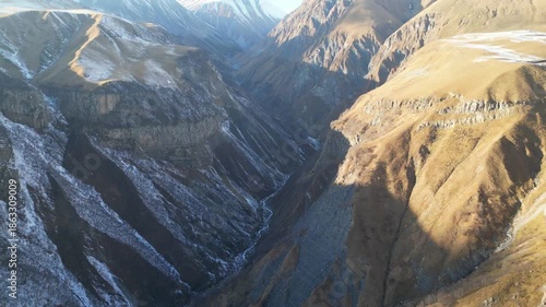 Aerial flight over Caucasus mountains near Gudauri Georgia. 4K horizontal drone footage shows massive Georgian peaks with snow-covered summits rising above rugged landscapes in clear sunny weather.