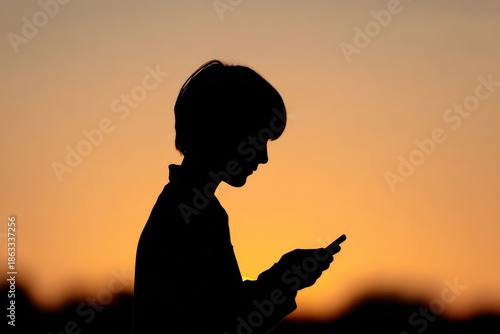 Teenage boy silhouette using smartphone against a vibrant sunset background, illustrating the concept of screen addiction and its impact on youth lifestyle and well-being