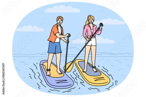 Surfing on SUP boards is practiced by man and woman using paddles to navigate river on summer weekend. Man and woman surfers stand on SUP boards, engage in active recreation at hot resort