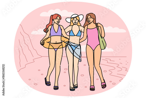 Women in bikinis walk along beach on seashore, enjoying summer holiday at hot resort. Three tourist girls pose on sandy beach, inviting you to visit tropical island to sunbathe and swim