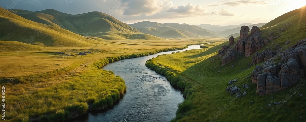 Fototapeta premium Green rolling hills and a winding river flow through a wide valley. Sunlight illuminates the grassy plains and rock formations under a cloudy sky. Natural landscape in open space.