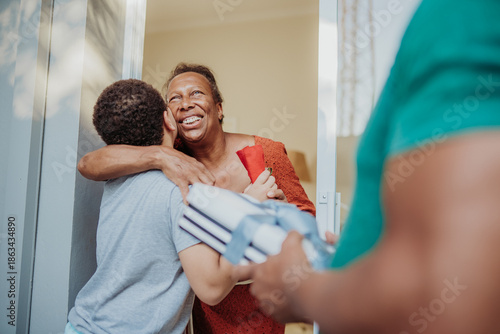 Obraz na płótnie Happy African American grandmother hugging her grandson at the front door while receiving a gift from family