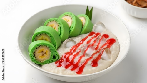 Traditional Indonesian Es Pisang Ijo: steamed banana wrapped in green dough, served with marrow porridge (bubur sumsum), red syrup, and ice cubes in a white bowl.
