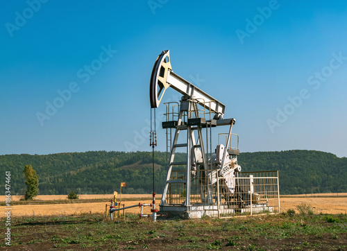 A large oil pump jack operates in an open field, extracting crude oil