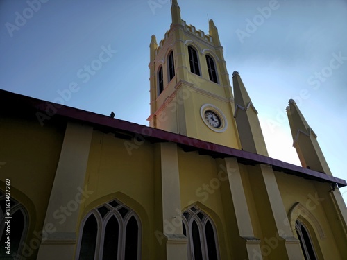 Low-angle view of Christ Church Shimla showing its tall clock tower and yellow facade against a clear sky, highlighting colonial-era architecture and historic charm.