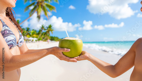 Close-up of Hands Holding a Fresh Coconut with a Straw on a Sunny Tropical Beach.Summer Vacation Concept