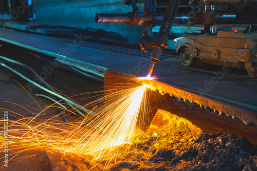 Acetylene torch semi auto machine cutting metalwork fabrication with bright sparks in factory.