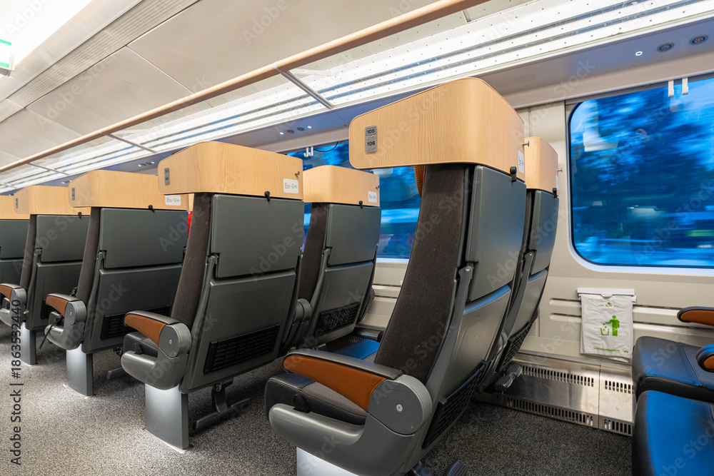 Obraz premium Empty modern train seats with wide windows and soft lighting, showing snowy scenery passing outside with motion blur, creating a calm winter travel atmosphere inside a clean passenger cabin.