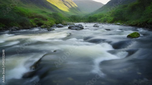 Moody long exposure photography highlights the rushing river water flowing over dark rocks, framed by lush green slopes in the comeragh mountains valley.