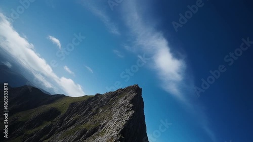 The sharp, rocky peak of the comeragh mountains dramatically juts into the vast deep blue sky, captured in a low-angle, diagonal wide shot emphasizing the adventurous high-altitude landscape.