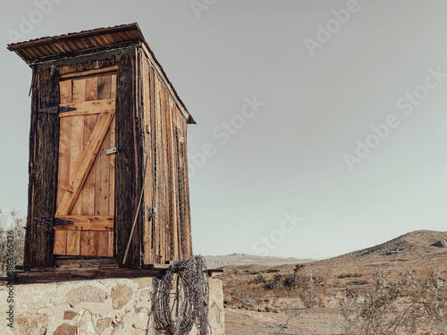 Fotografi A small wooden outhouse with a slanted roof stands on a stone base under a clear