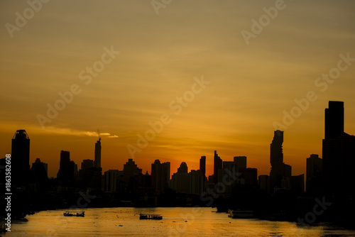 Stunning city skyline silhouette at sunset with golden sky reflecting on water, creating serene and peaceful atmosphere