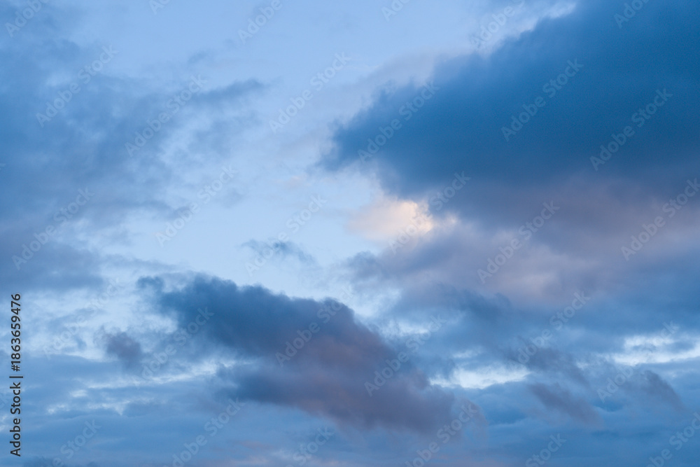 Obraz premium Layered blue and lavender clouds drift across a tranquil evening sky, with soft gradients and gentle light creating a calm, atmospheric scene.