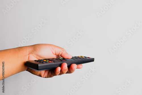 Close-up of a human hand holding a TV remote control isolated on white background, representing home entertainment, television, streaming, technology, and leisure lifestyle.