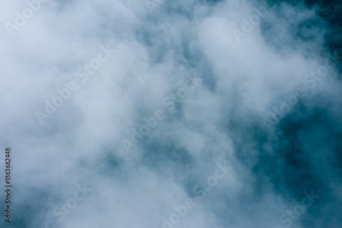 Billowing white clouds drift over a blue background, creating an abstract, minimal composition with gentle gradients and soft textures. The image evokes a tranquil, airy mood and a sense of calm