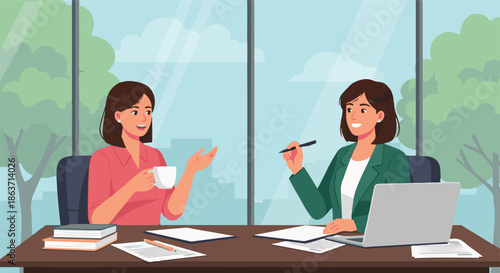 Two women collaborating at a desk in an office setting, discussing work over coffee