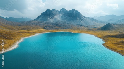 Vibrant Blue Lake Reflecting Rocky Mountains Amidst Golden Fields Under a Cloudy Sky